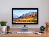 iMac computers, iPhone, iPad, plant vase, cactus, pencils and clock on wooden table.