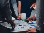 A group of businesspersons meeting with various printed graphs and charts on a table.